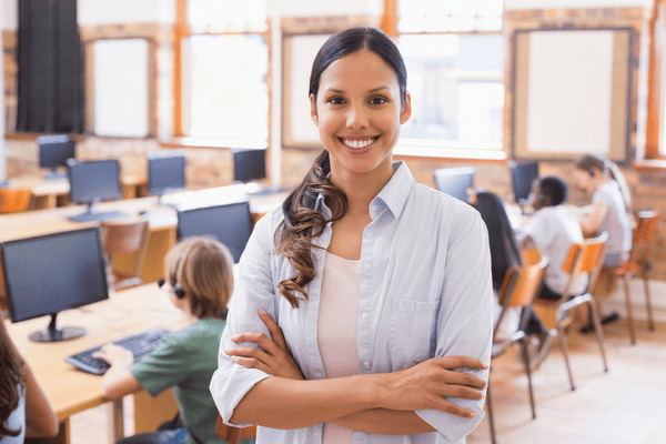 A teacher smiling in her classroom while students work on computers, showcasing an environment supported by school Medicaid billing revenue.